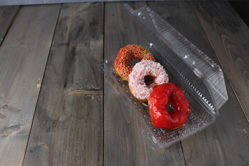 Three red donuts in a plastic box on a gray background with space for copyspace text. Donut Day Candy Delivery American Food