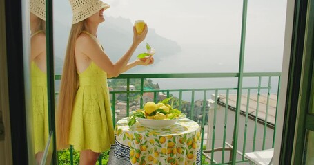 Woman in a yellow dress savours a lemon sorbet or ice cream on a balcony. Overlooking the Amalfi coastline, the moment is serene and picturesque.