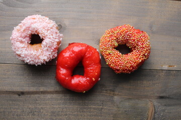 Three donuts red, pink, white, glazed on a gray background with space for text. Donut Day is sugar food. Sugar in Foods Bad Carbohydrates