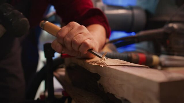 Craftsperson carving into wood using chisel and hammer in carpentry shop with precision. Manufacturer in studio shaping wooden pieces with tools, making wood art, camera B close up shot