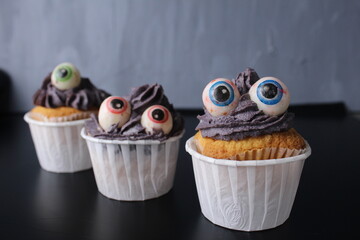 Three cupcakes on a black background for the Halloween holiday. Scary and funny food. Sweets for the holiday