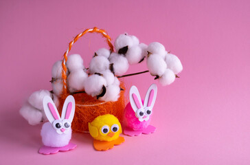 A branch of white cotton, toy eggs with birds in an orange basket and Easter bunnies on a pink...