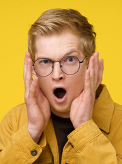 A man with glasses is screaming on a yellow background. The man's facial expression and the color of his jacket create a sense of urgency and excitement