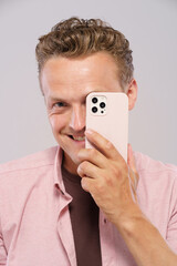 A man is holding a pink iPhone in front of his face. He is smiling and looking at the camera