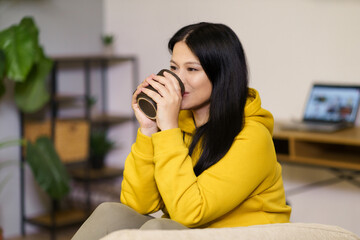 A woman in a yellow hoodie is drinking coffee. She is smiling and she is enjoying her drink