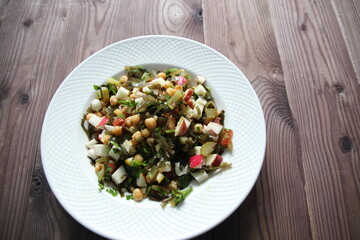 Salad with laminaria, chickpeas, vegetables in white plate on brown wooden table