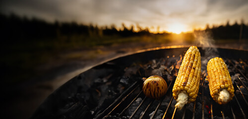 corn and onions on a wood and charcoal grill - smoke and flames char the corn kernels creating delicious colors, textures and flavors for a vegetarian bbq side item entree outdoor cooking, open fire - obrazy, fototapety, plakaty