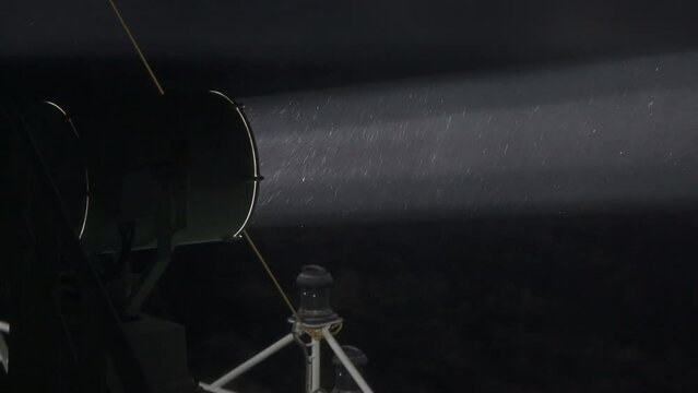 Searchlight beam in a snowstorm at night. Close up. Big searchlight on ship