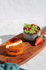 A portion of fresh made fried camembert cheese with cranberry sauce on top and a side of fresh salad on wooden plate