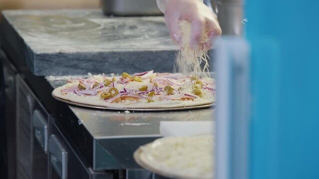 Close Up Of Chef Adding Olives And Cheese To Cook Tasty Pizza Food. Sprinkling Cheese On Tasty Italian Cuisine Food. Shredded Cheese Ingredient. Tasty Food Preparation. Delicious Recipe