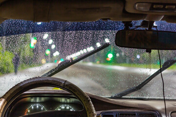 view from the inside of a working car at night on an illuminated road during heavy rain and...