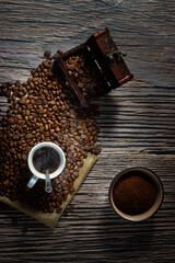 Top view of a cup of coffee between selected roasted coffee beans an a bowl of freshly ground...