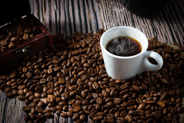 A cup of coffee between selected roasted coffee beans on wooden background.