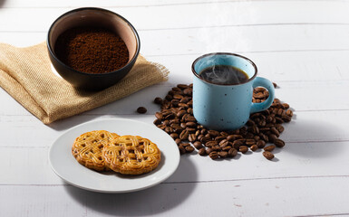 Freshly brewed coffee cup, homemade cookie and freshly ground coffee on white wooden background.