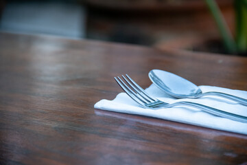 Spoon and fork on a brown wooden table. Table layout in a restaurant or hotel with utensils before...
