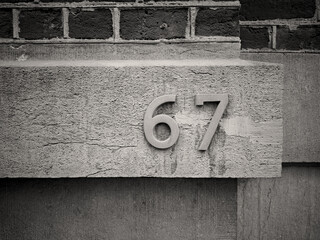 Metal painted number sixty seven or 67 applied in Latin letters to the building. Black and white...
