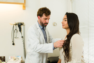 Handsome doctor using the stethoscope on a female patient - 778535885