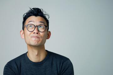 Decision, thinking and Asian man in studio with glasses, questions and brainstorming on grey background. Why, idea and male person with emoji, body language or choice gesture, puzzled or solution - obrazy, fototapety, plakaty