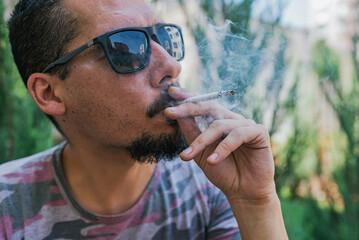 Handsome Man Smoking a Cigarette Outdoor In a Sunny Day - obrazy, fototapety, plakaty