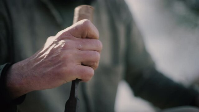 Carpenter using mallet and chisel for wooden cross made by hand in sunlight.