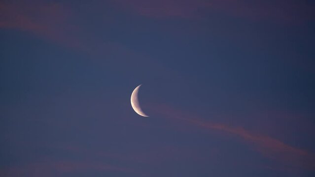 Sunrise timelapse of a Waning Crescent Moon as pink clouds move by at dawn.