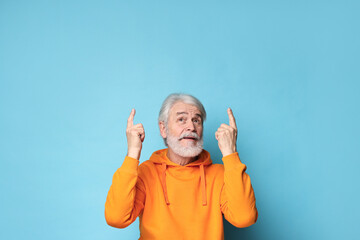 Senior man with mustache pointing at something on light blue background