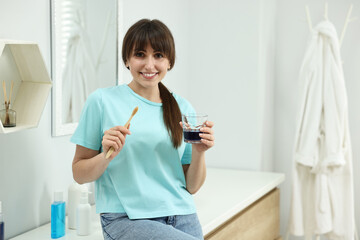 Young woman with mouthwash and toothbrush in bathroom