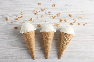 Fotobehang Ice cream scoops in wafer cones on light wooden table, flat lay © New Africa