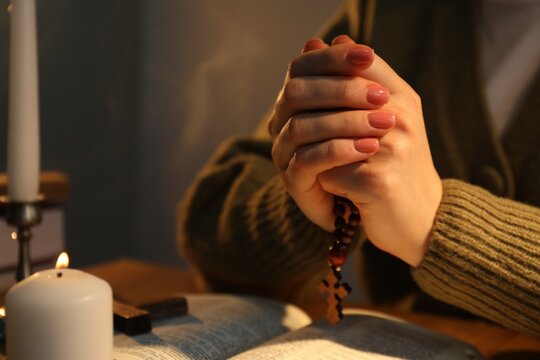 Woman praying at table with burning candle and Bible, closeup