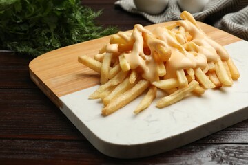Delicious french fries with cheese sauce on wooden table, closeup
