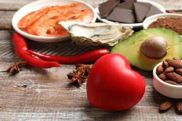 Natural aphrodisiac. Different food products and heart model on wooden table, closeup