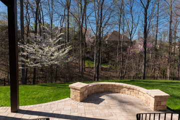 Picturesque backyard view in spring season with patio pavers and stone wall, blooming white cherry...