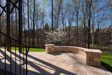 Picturesque backyard view in spring season with patio pavers and stone wall, blooming white cherry...