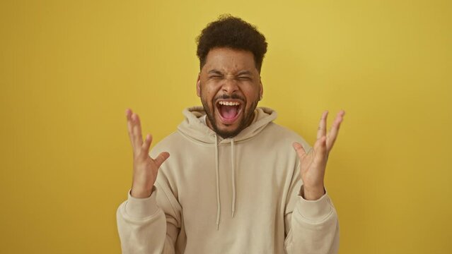 Excited african american man in a hoodie going mad with joy, celebrating a crazy success win with arms flung wide! winner vibes on a yellow isolated background.