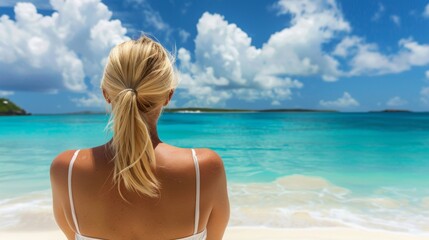 A blonde woman in a white bikini standing on a beach, gazing out at the ocean