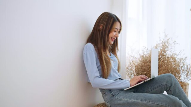 Young asian woman working at home. Happy female using computer laptop in living room at house
