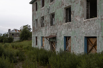 View of abandoned old houses in a provincial town. Broken and boarded up windows. Peeling cracked paint on the wall of a building. Overgrown city yard. Dilapidated buildings.