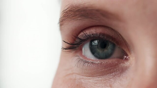 Blinking, half and eye for health of vision, closeup and sight for looking in white background. Studio, person and adult with cosmetics of microblading of eyebrow on face with care for beauty