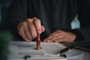 Focused individual placing a seal on an official document with red wax stamp in a professional...