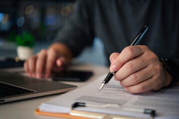 A businessman's hands with a pen over documents, analysis at the workplace.