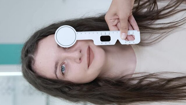 Attentive optometrist examining a beautiful female patient, testing her vision using a ruler to determine interpupillary distance with an occluder in an ophthalmology clinic. Examination in a clinic
