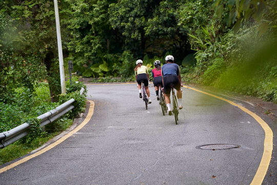 rear view of three young professional asian cyclists riding bike training outdoors on rural road