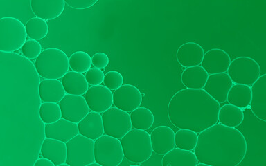 Abstract oil serum droplets on water surface to creates bubbles and an  art  pattern with green background. 