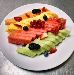 Freshly cut fruits neatly arranged on a white ceramic plate.
