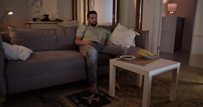 Lazy man watching TV and drinking beer in living room at home