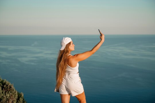 Selfie woman in a cap, white tank top and shorts makes a selfie shot mobile phone post photo social network outdoors on the background of the sea beach people vacation lifestyle travel concept.