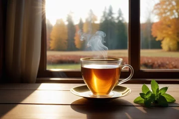 Poster A glass cup of hot tea with mint leaves on a wooden table beside a window, cozy background, horizontal composition © Thanh