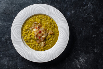 Green pea mash with fried onions in a white plate with spices on the table, closeup, top view. Healthy food, delicious dried green peas soup - 778650649