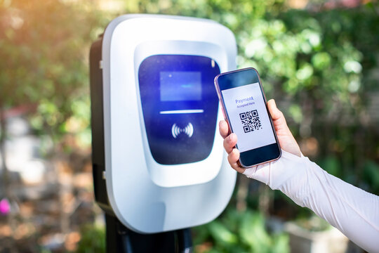 EV Driver use smartphone to scan QR Code on electric vehicle charging stations to pay for electricity. The concept of QR scanning payment instead of cash.