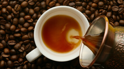 Turkish coffee is poured into a white coffee cup on the background of coffee beans, close-up. Top view, flat lay composition.